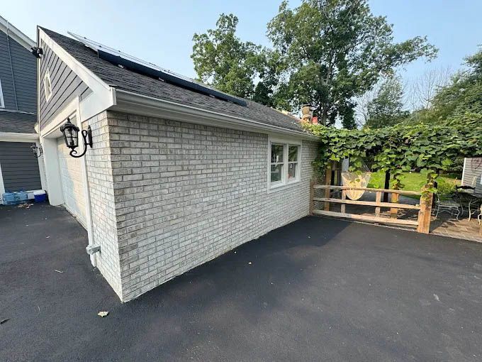 A white brick garage with a wooden fence and solar panels on the roof.