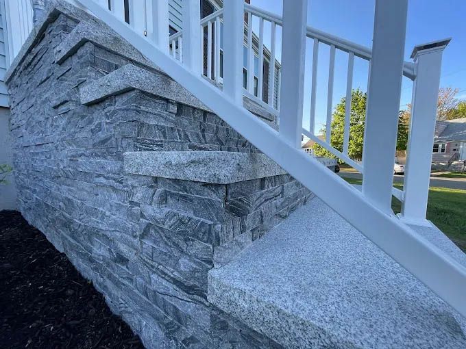 A set of stairs with a stone wall and a white railing.