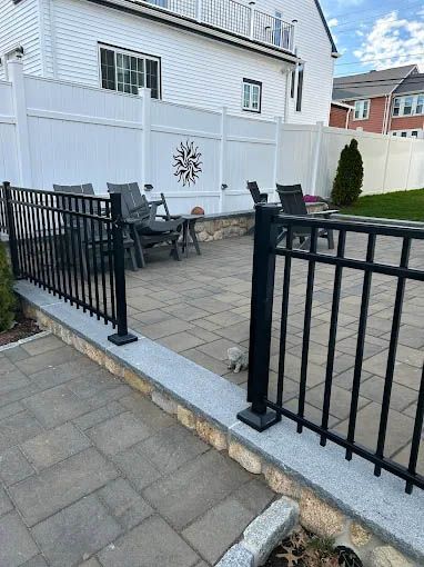 A black fence surrounds a patio with chairs and a table.