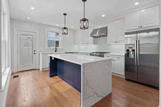 A kitchen with a large island , stainless steel appliances , white cabinets and hardwood floors.
