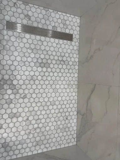 A shower with a honeycomb tile floor and a drain.