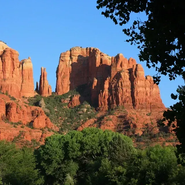A mountain with trees in the foreground and a blue sky in the background