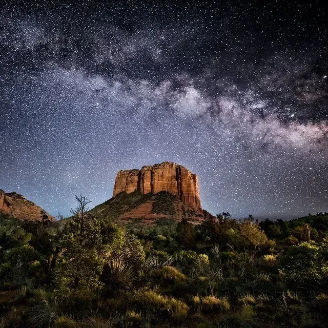 There is a mountain in the foreground and a milky way galaxy in the background.