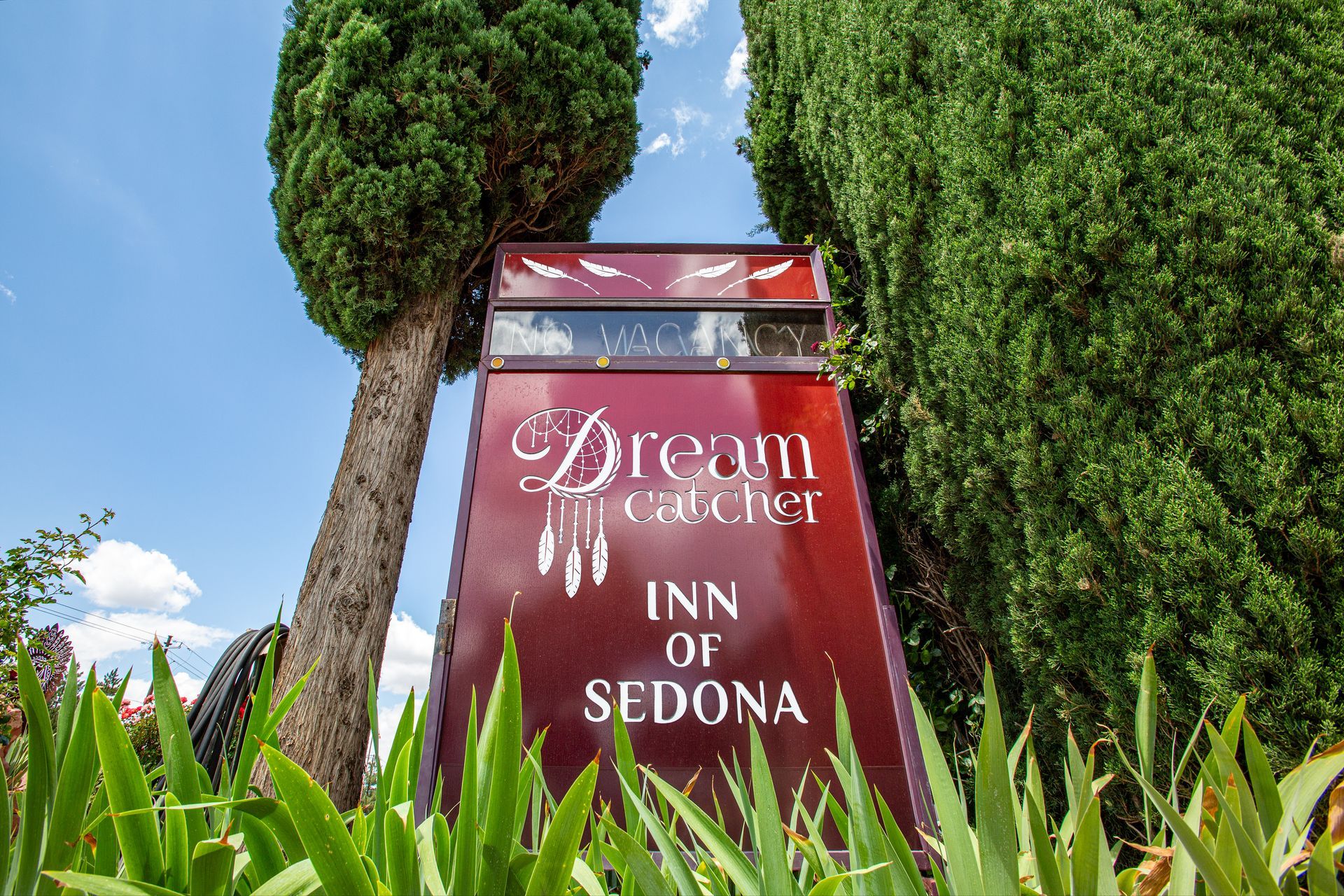 A red sign for the dream inn of sedona is surrounded by trees.