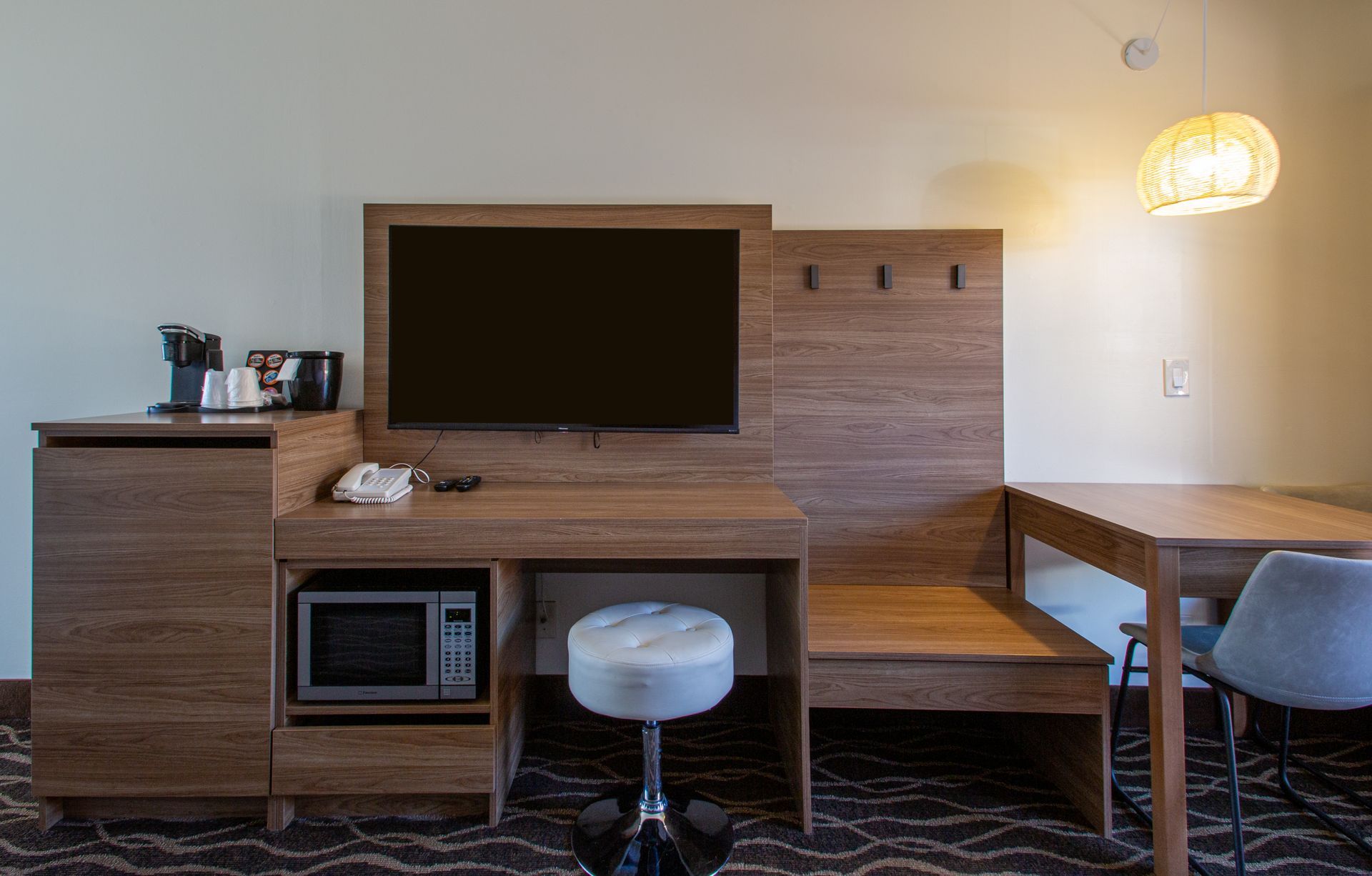 A hotel room with a desk , table , chairs , television and microwave.