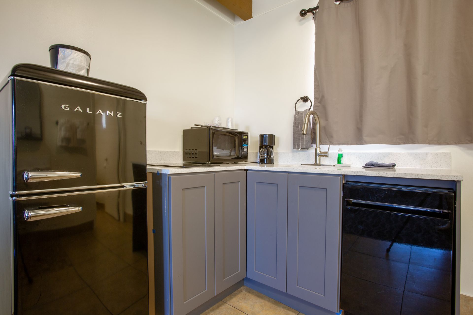 A kitchen with a black refrigerator , gray cabinets , and a black dishwasher.