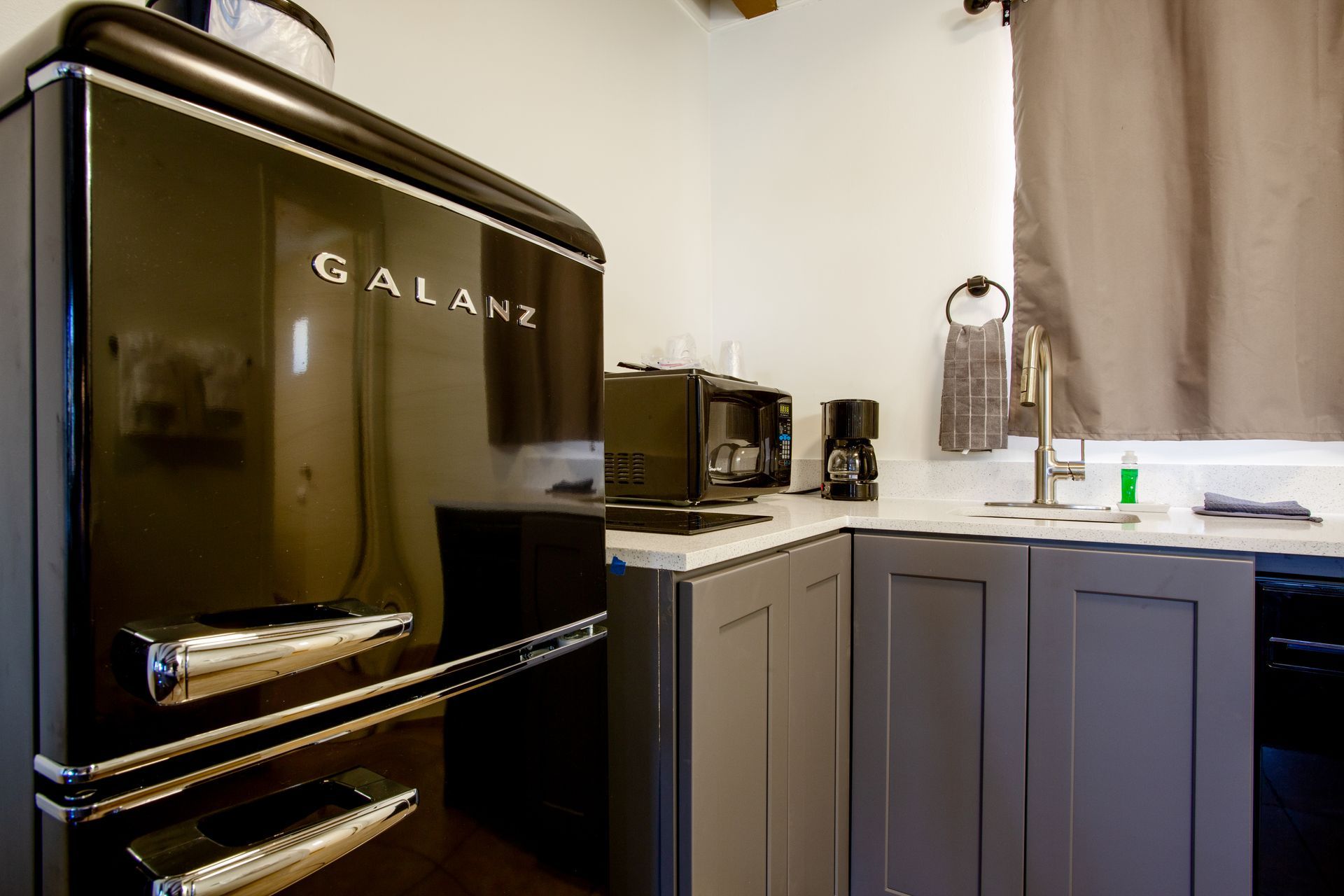 A black refrigerator is in a kitchen next to a sink.