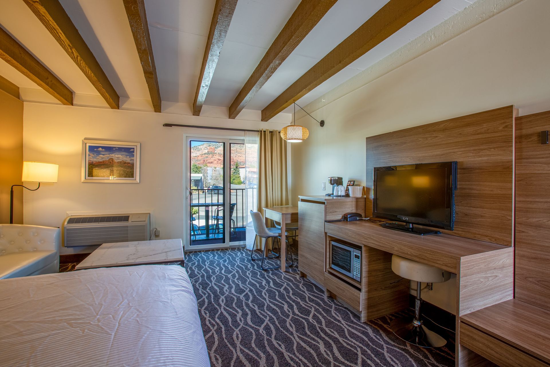 A hotel room with a bed , desk , television and balcony.