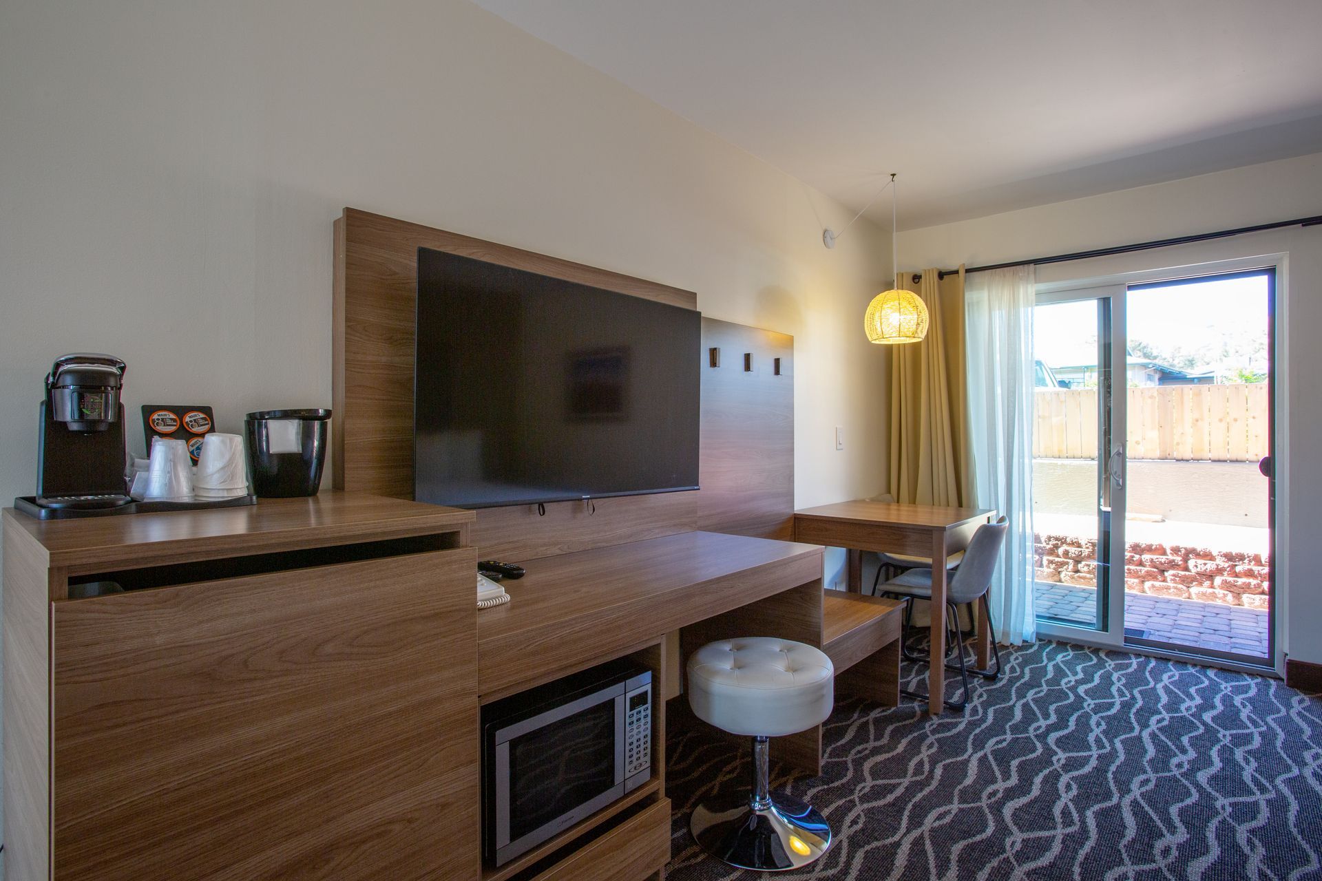 A hotel room with a flat screen tv , microwave , desk and chairs.