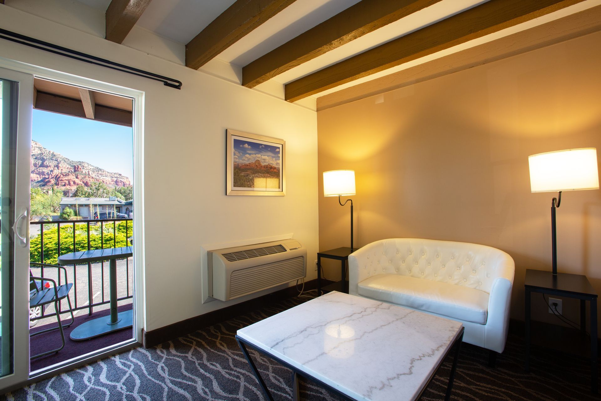 A hotel room with a couch , chair , table and balcony.