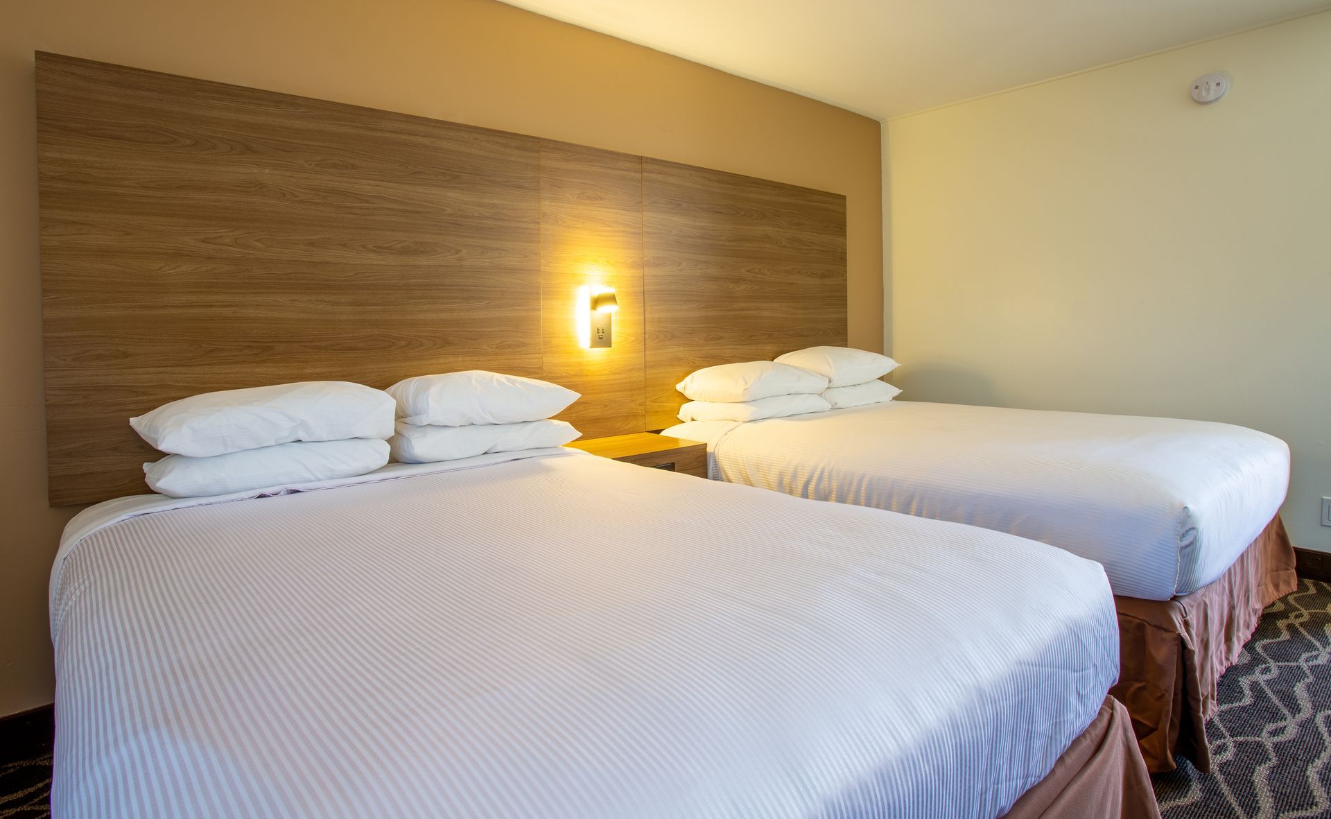 A hotel room with two beds and a wooden headboard.