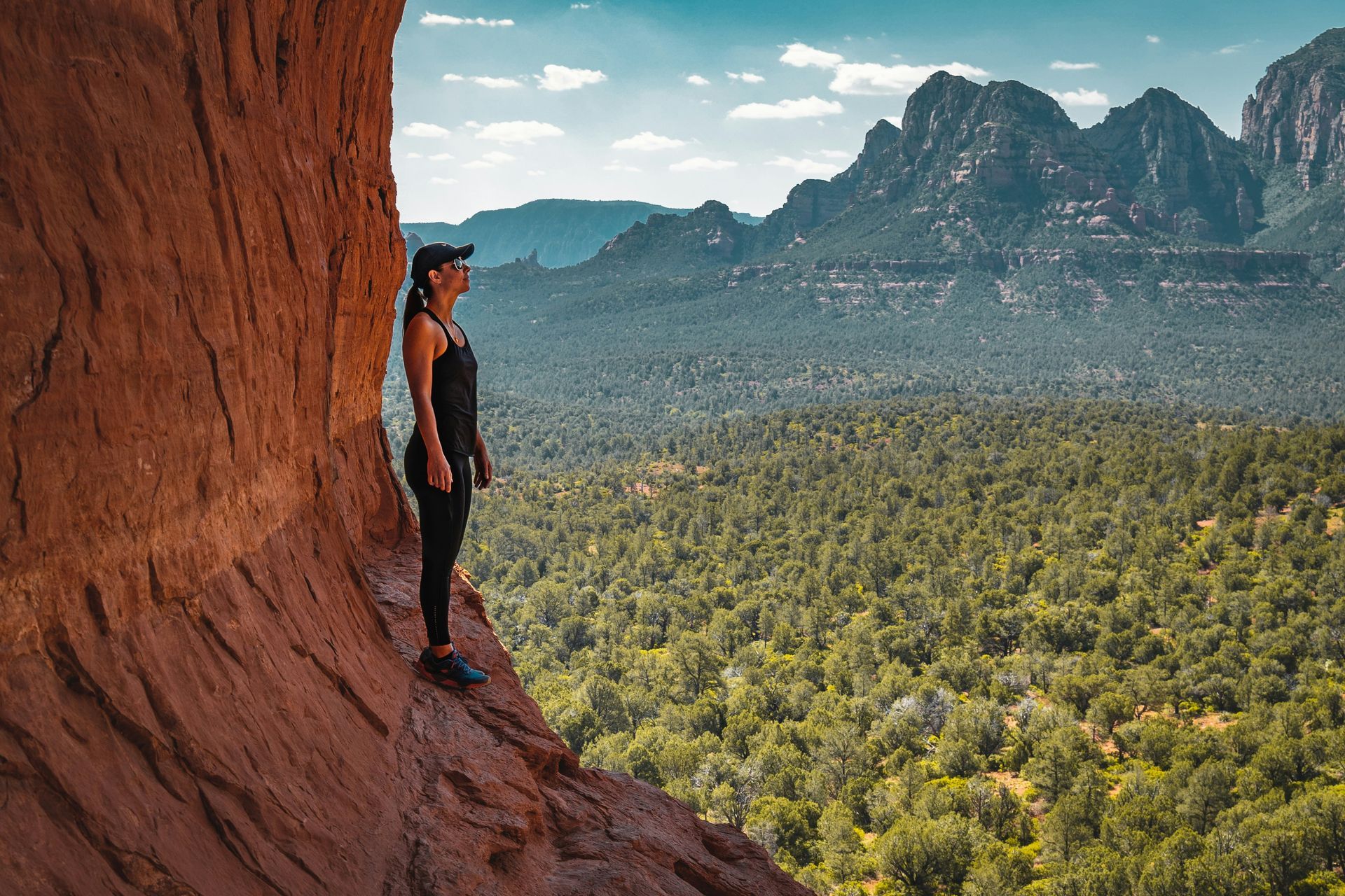 A woman is standing on the edge of a cliff overlooking a lush green forest.