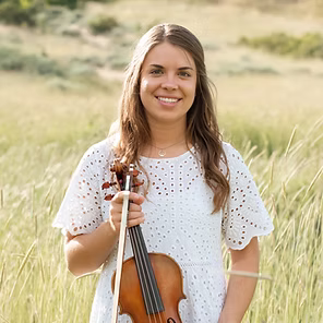 Young woman in a white dress holding a cello outdoors in a grassy field