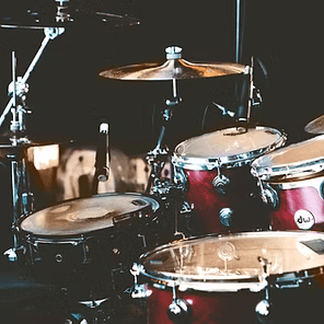 Drum kit on a dimly lit stage, with cymbals and red tom drums ready for performance