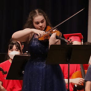 Violinist in a blue dress performing onstage with seated orchestra members behind her