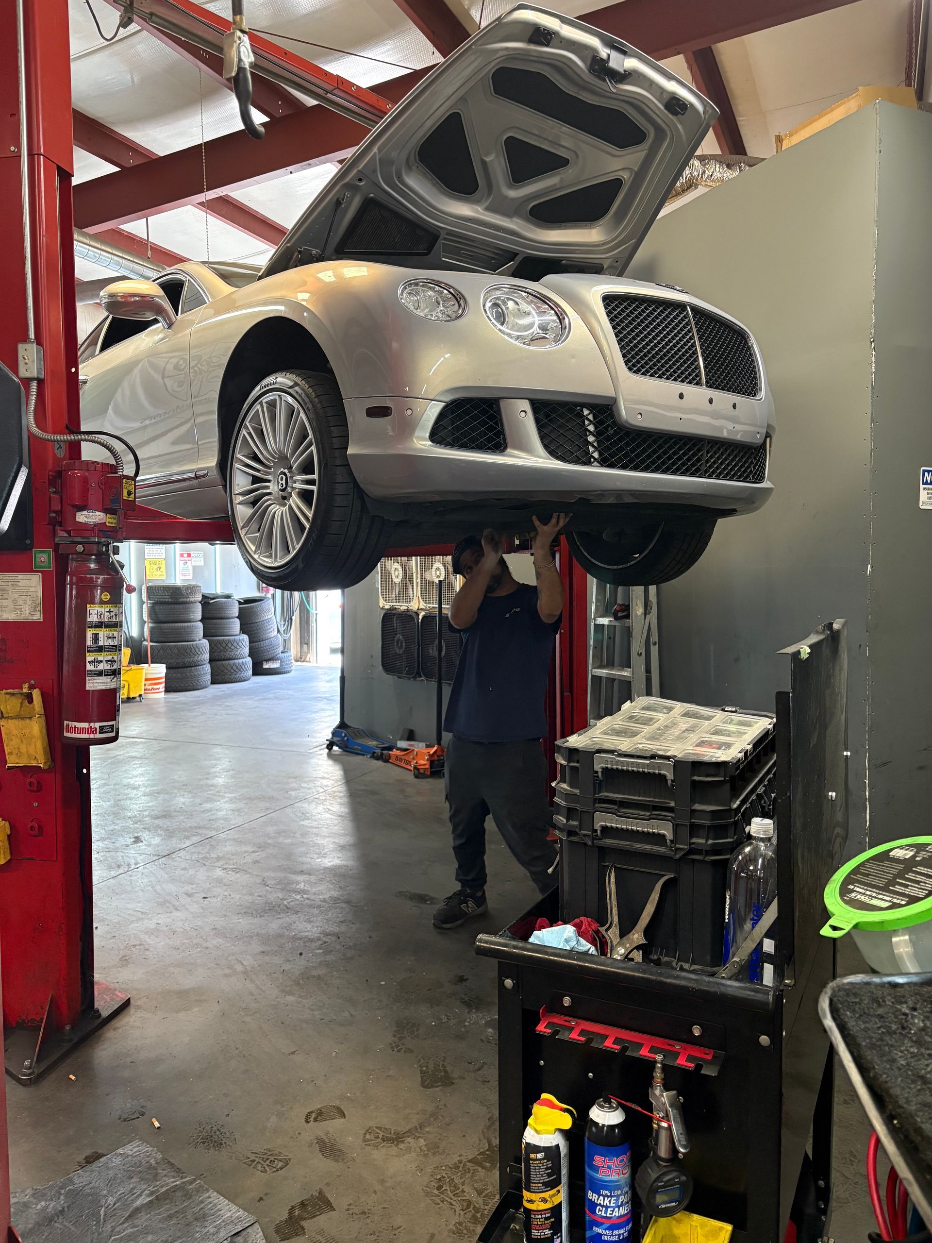A man is working on a bentley on a lift in a garage. | Platinum Motors Martinez