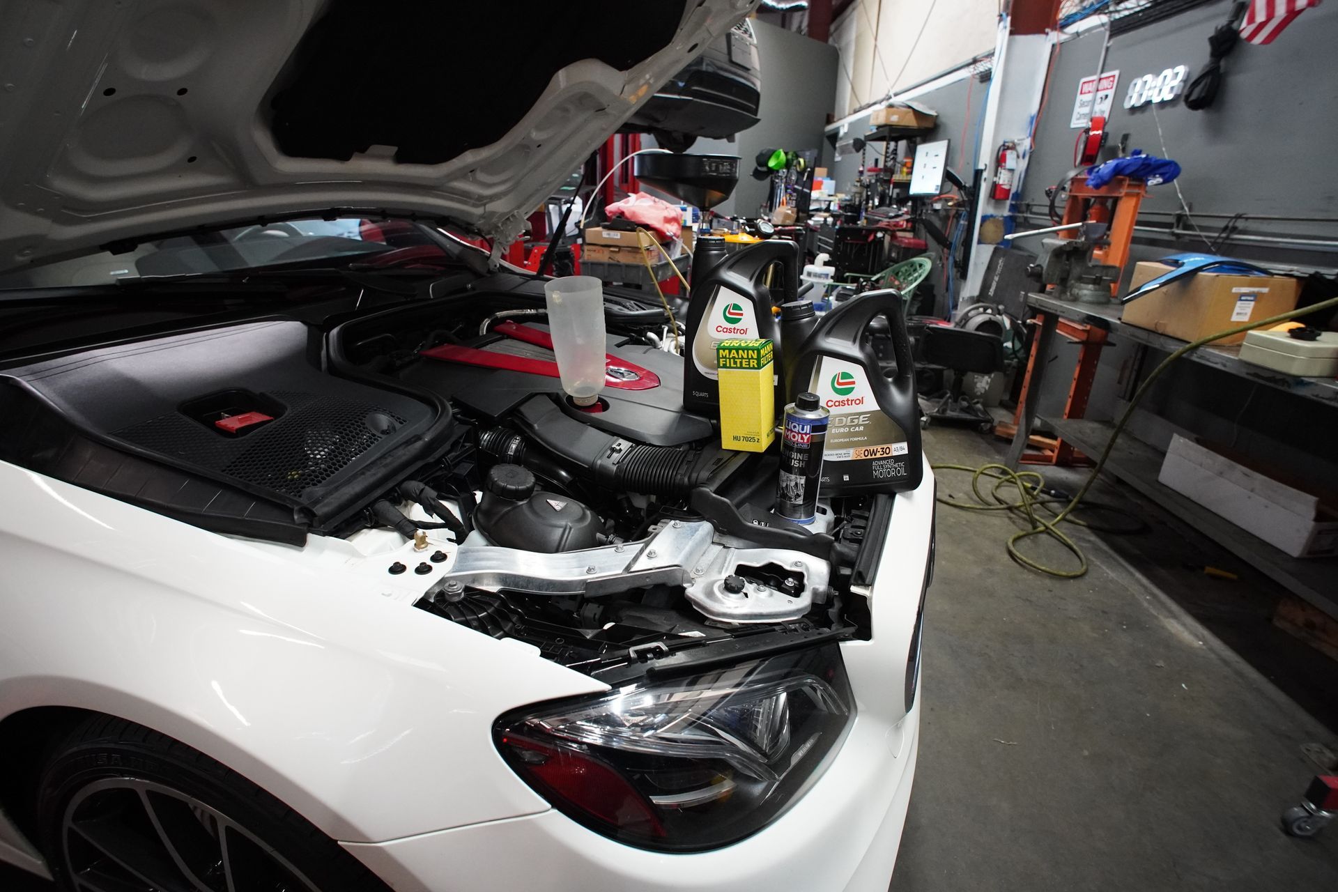White car with open hood, oil change supplies in a garage. | Platinum Motors Martinez