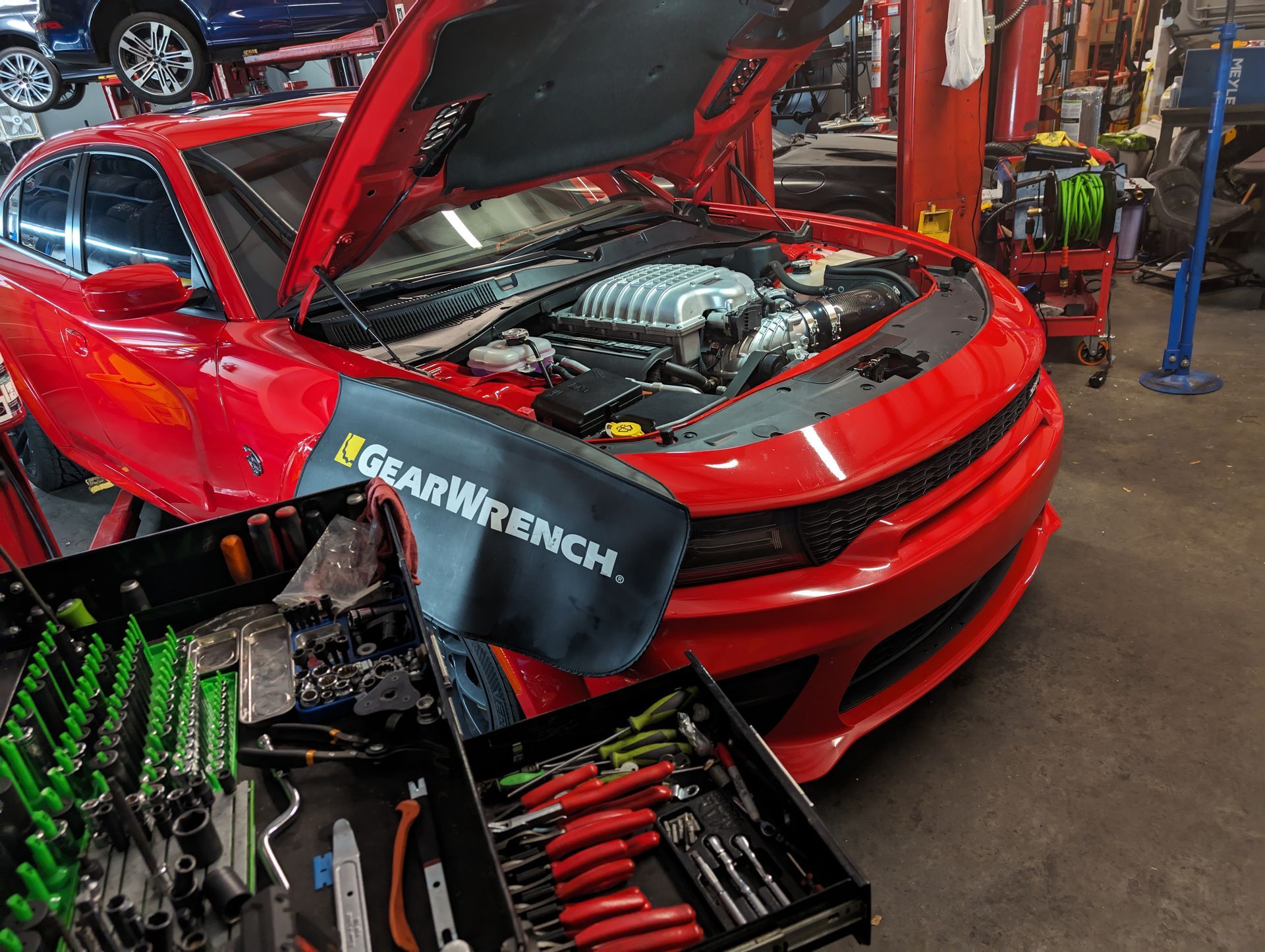 Red car with open hood in a garage; toolbox in front. | Platinum Motors Martinez