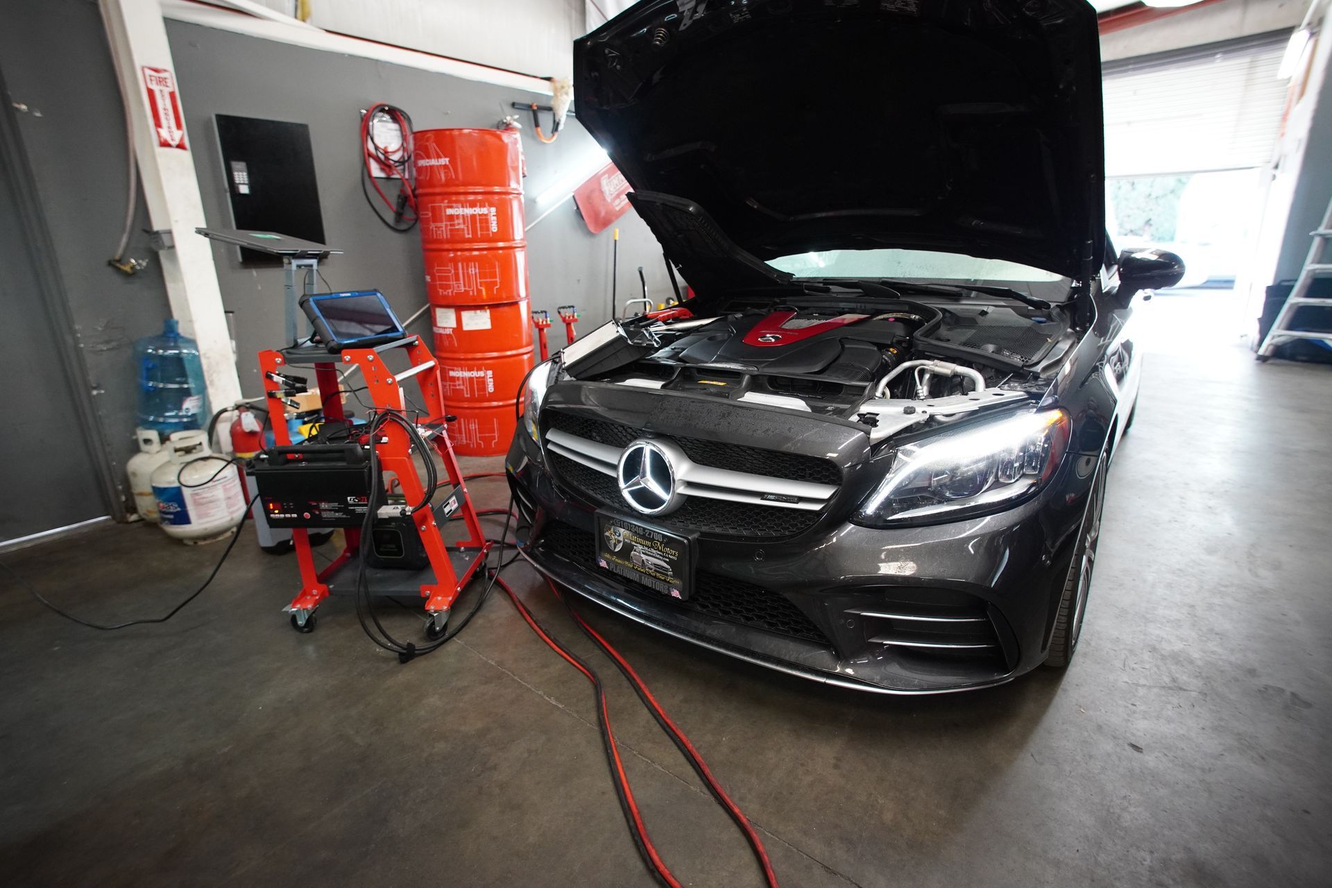 Dark Mercedes-Benz with open hood in a garage, undergoing diagnostic checks, hoses and equipment visible. | Platinum Motors Martinez