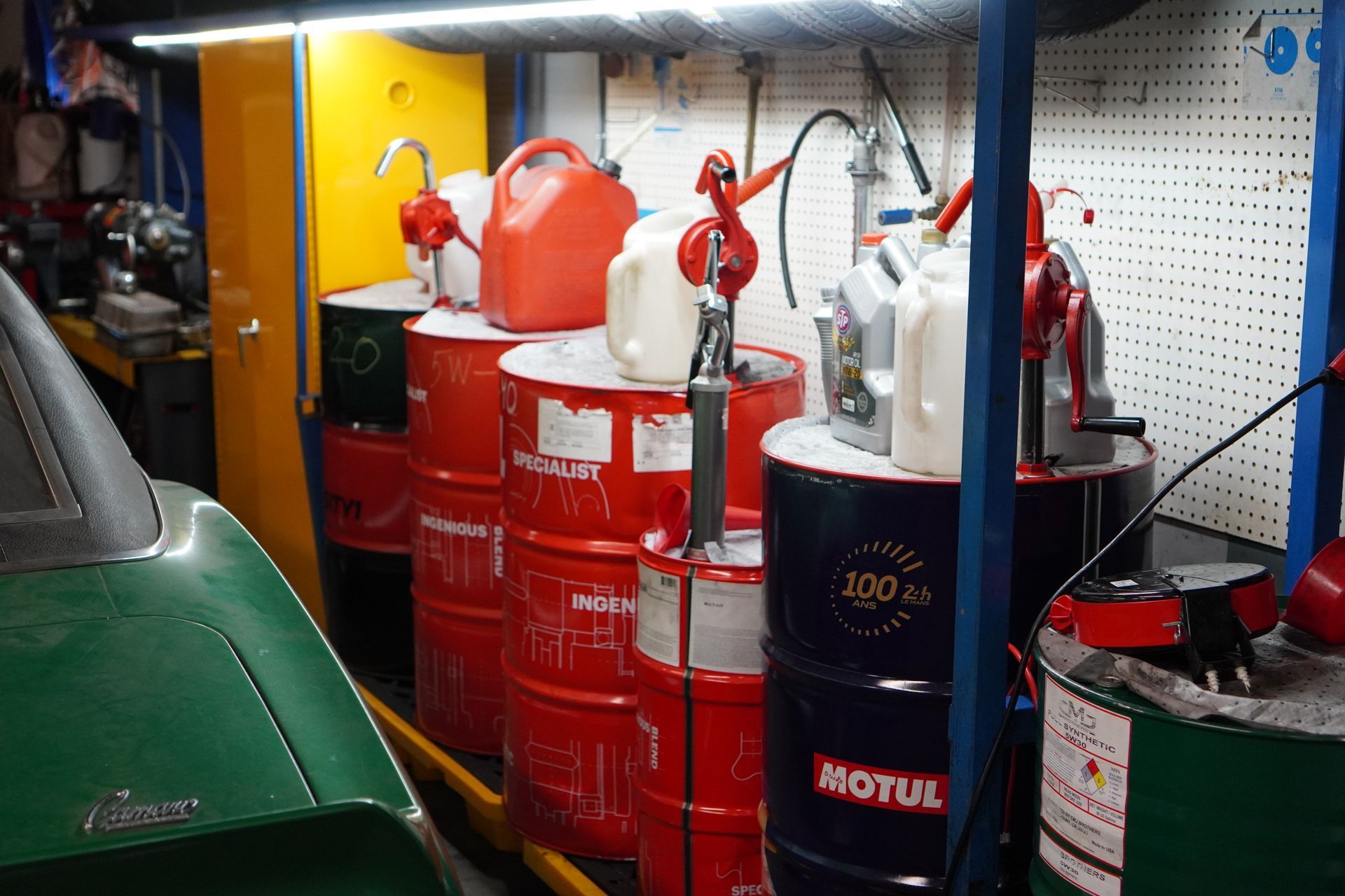 Red and black oil barrels with hand pumps in a garage. Green car visible. | Platinum Motors Martinez