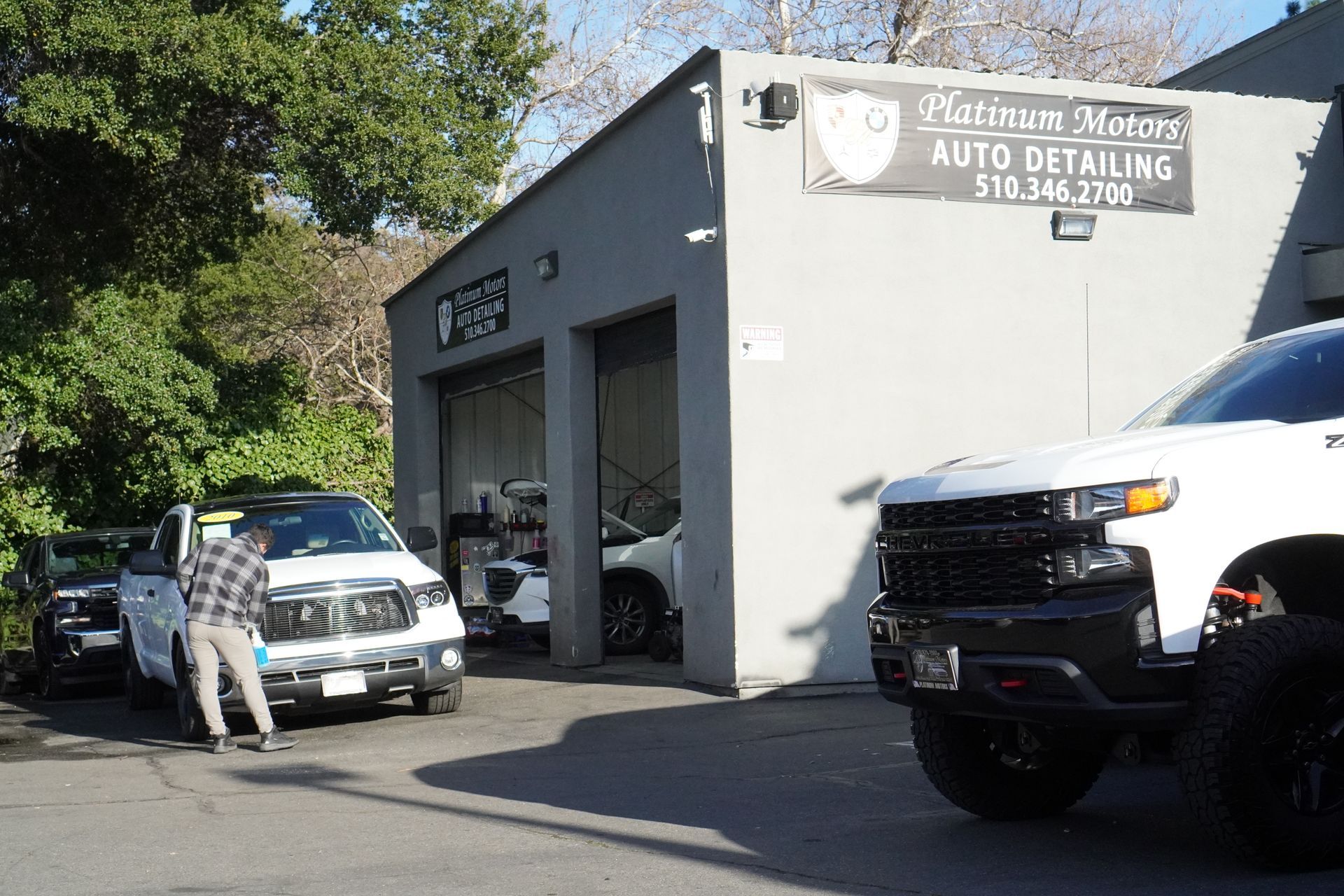 Platinum Motors auto detailing shop with trucks, and a person near a vehicle. | Platinum Motors Martinez