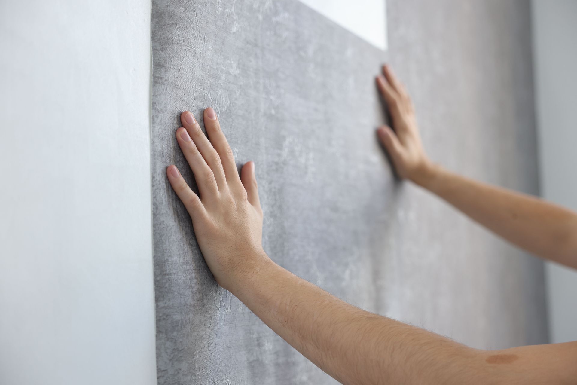Hands smoothing gray wallpaper onto a white wall.