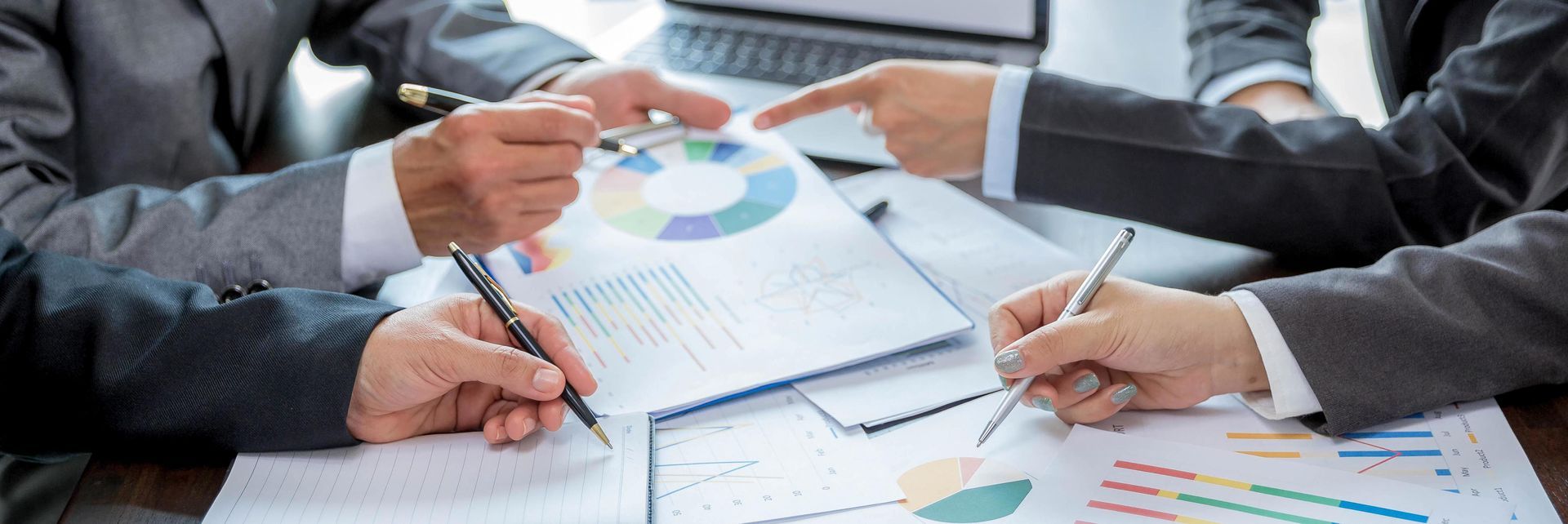 People in business suits review charts and graphs at a table.