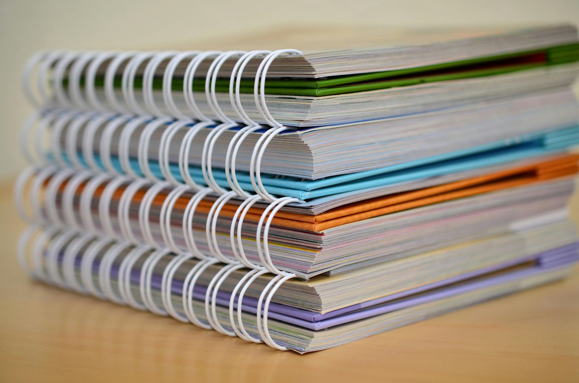 Stack of notebooks bound with white coils, each with a different colored cover peeking out.