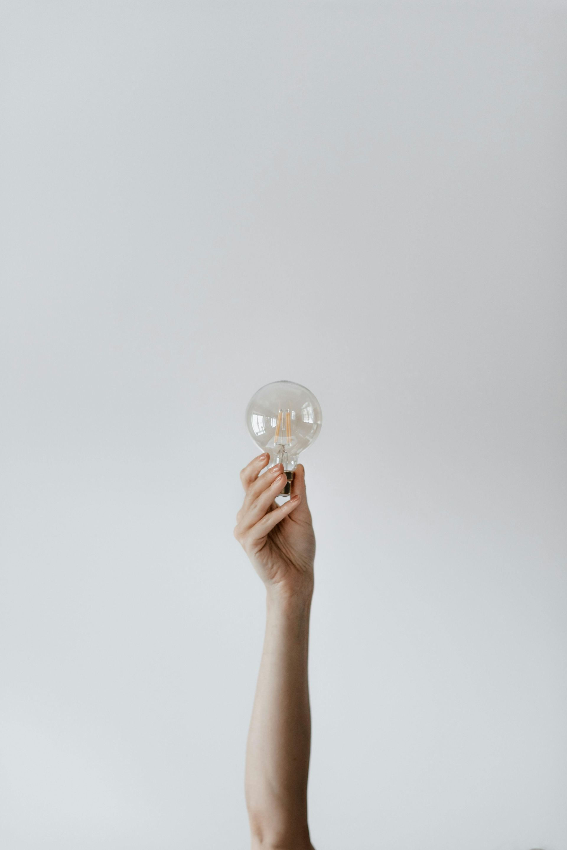 Arm raised, holding a lit lightbulb against a white background, symbolizing an idea.
