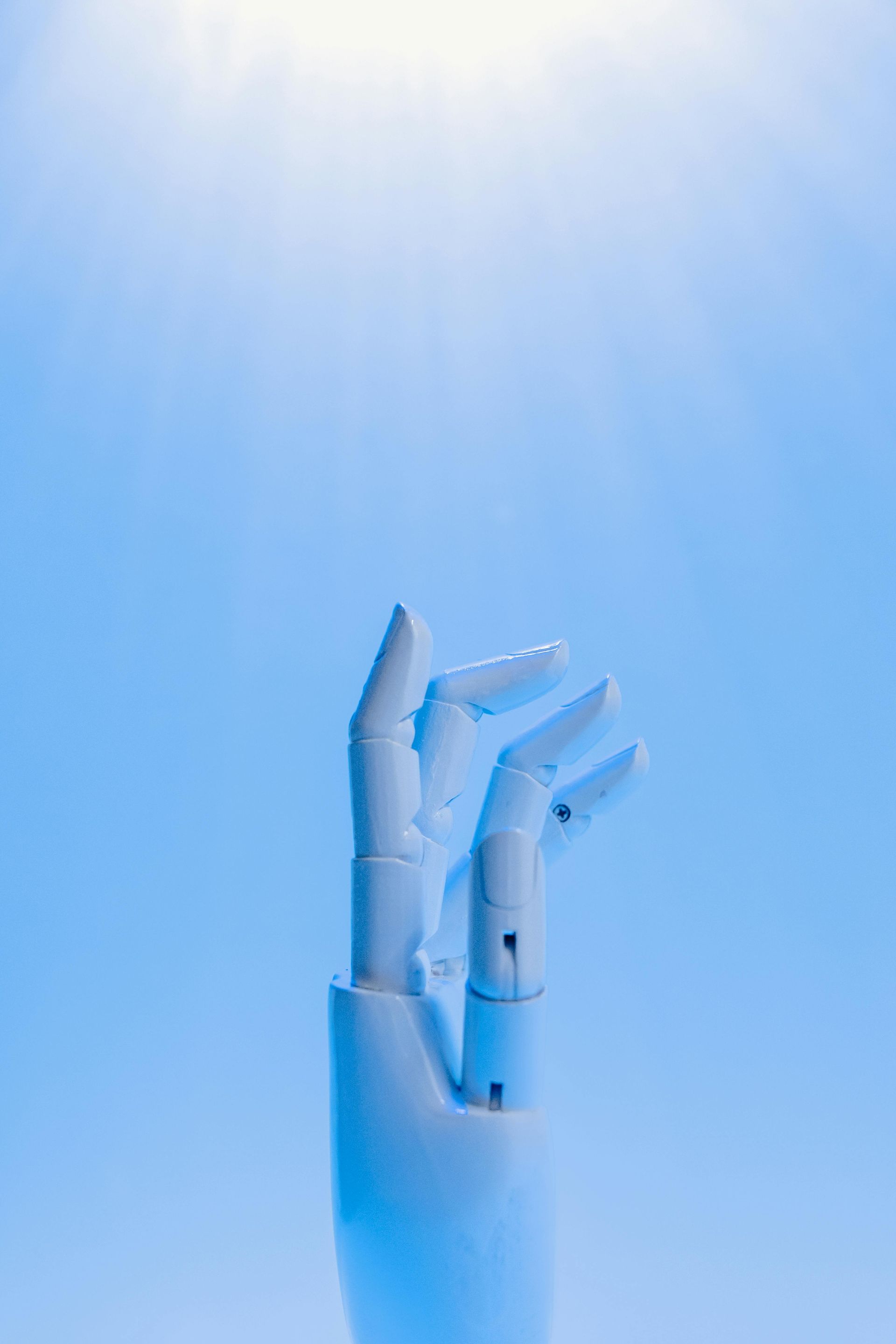 White robotic hand reaching up against a bright blue sky, fingers partially curled.
