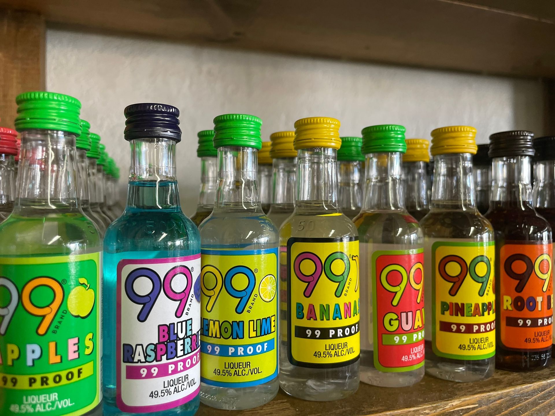 A bunch of bottles of alcohol are lined up on a shelf.