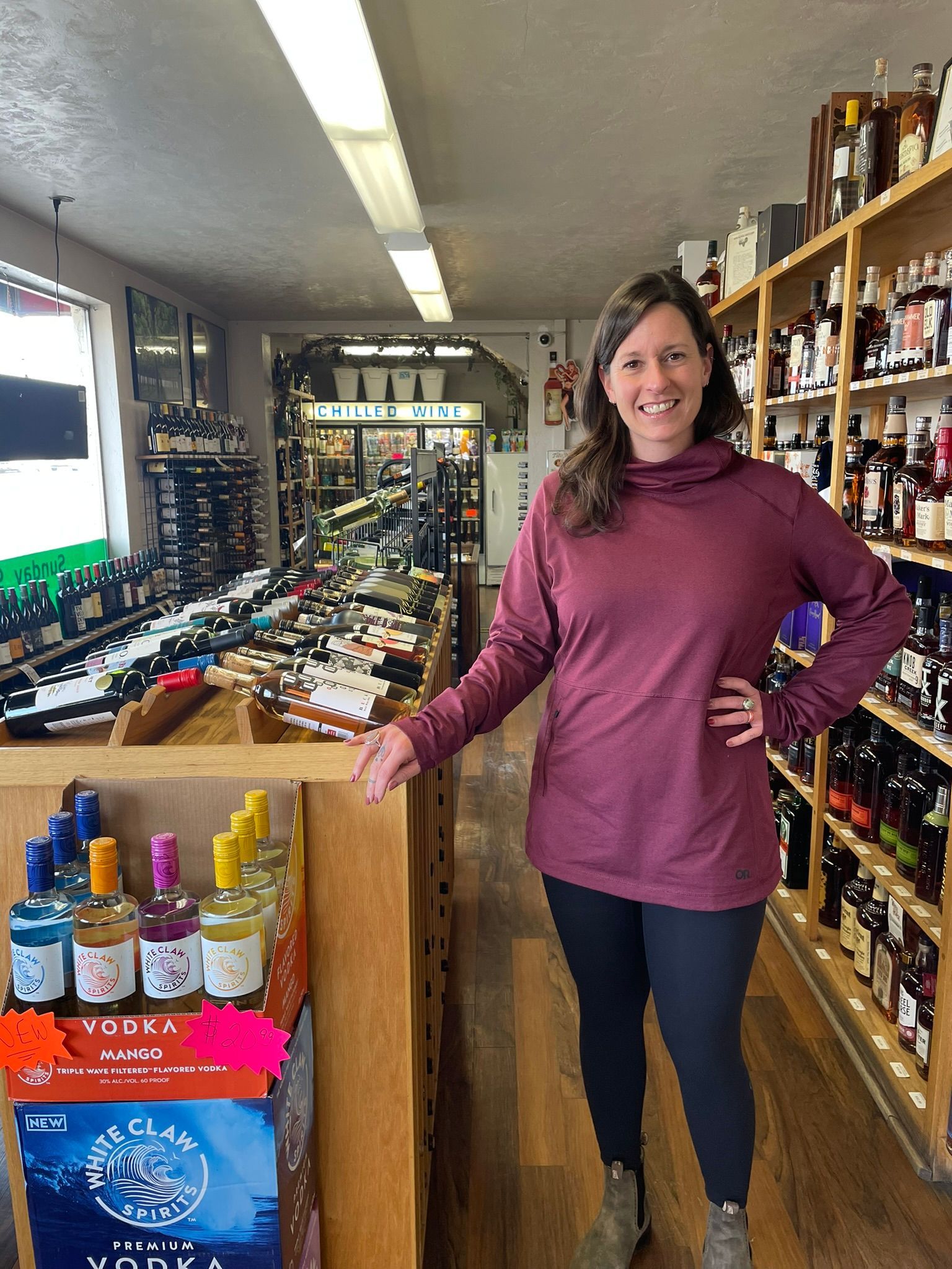 A woman in a purple shirt is standing in a wine store.