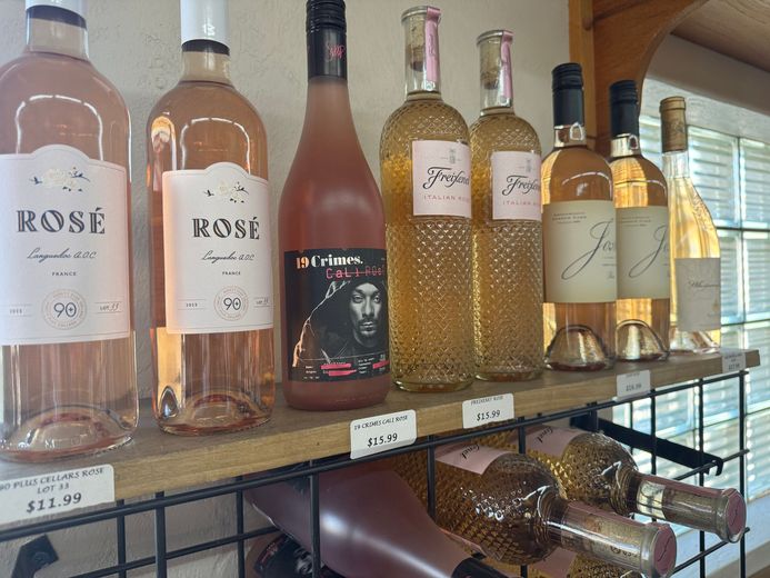 A row of wine bottles are lined up on a wooden shelf.