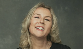 A woman with blonde hair is smiling and wearing a black shirt.