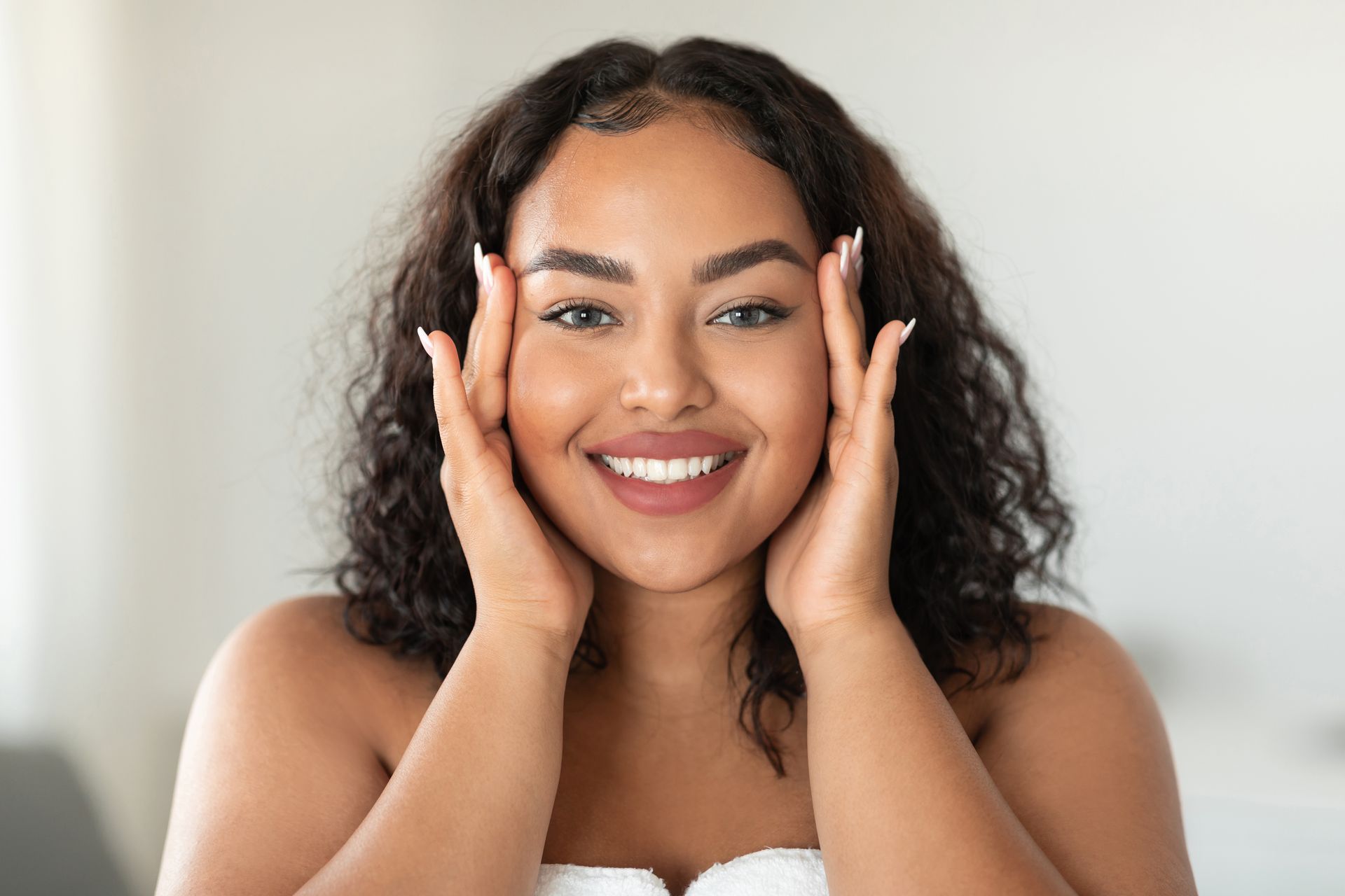 A woman is smiling and touching her face with her hands.