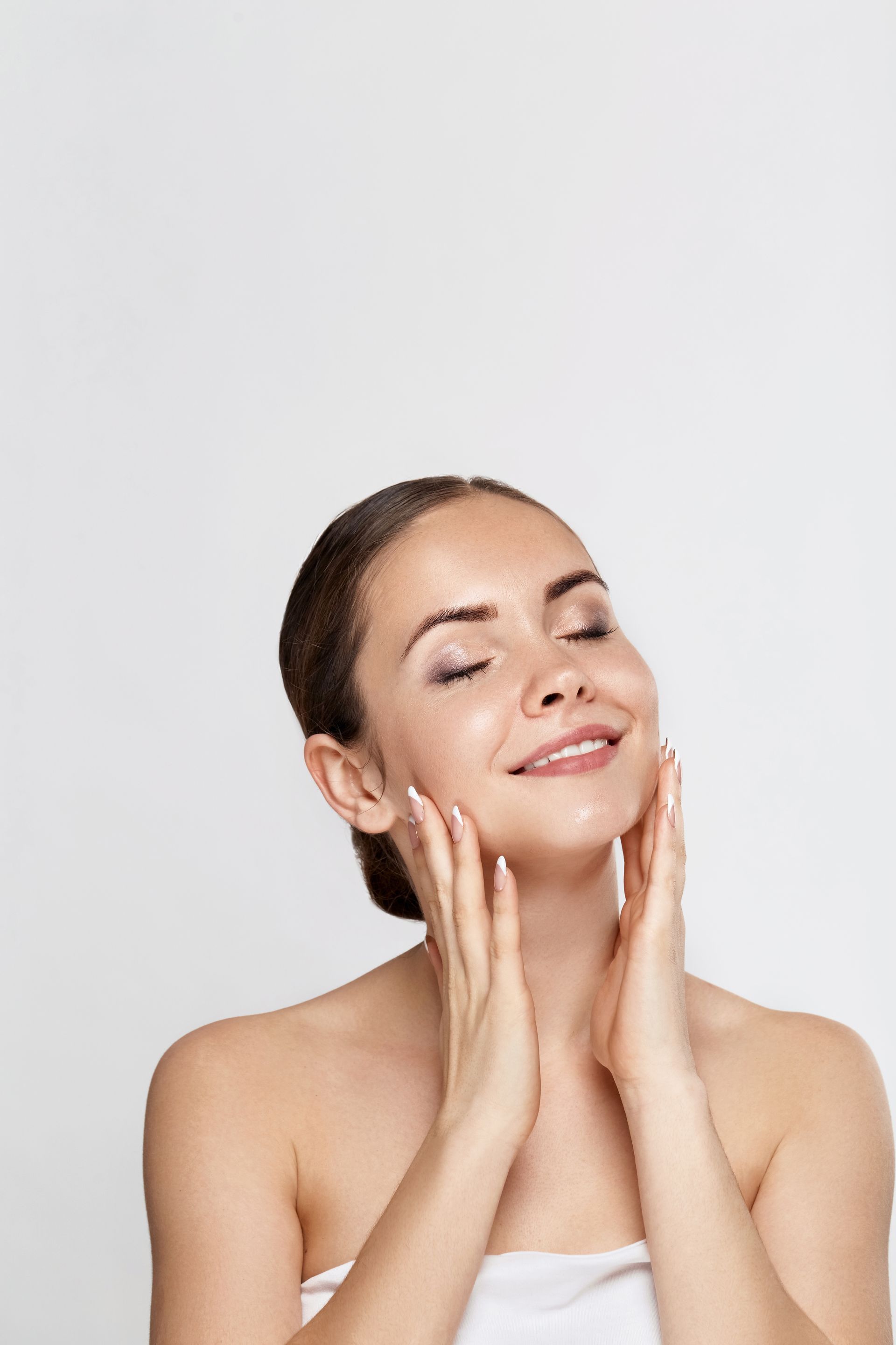 A woman is touching her face with her hands and smiling.