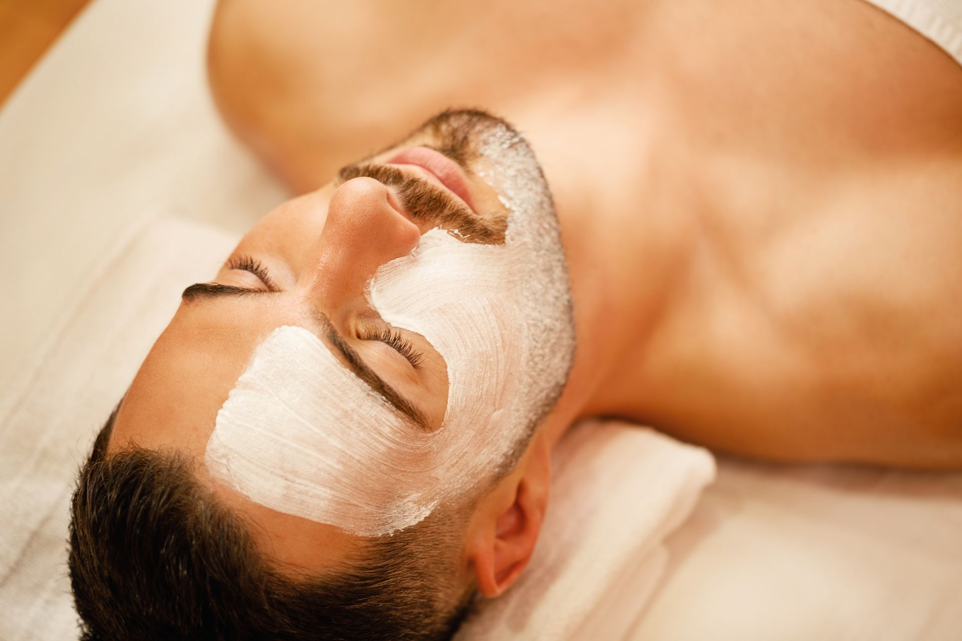 A man is laying on a bed with a white mask on his face.