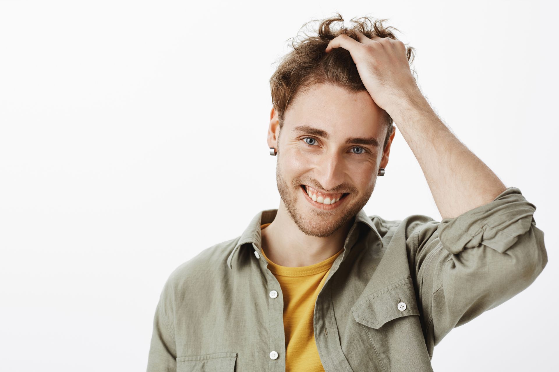 A man with a beard is smiling and touching his hair.