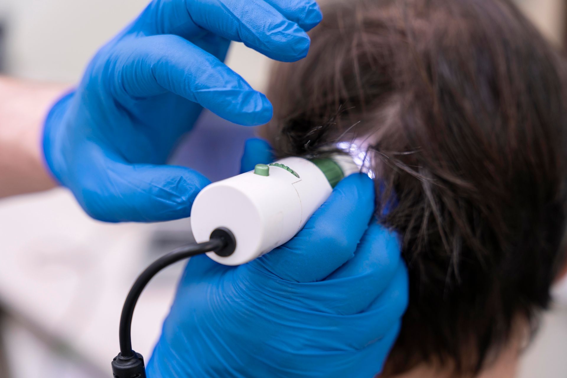 A person wearing blue gloves is examining a child 's hair with a microscope.