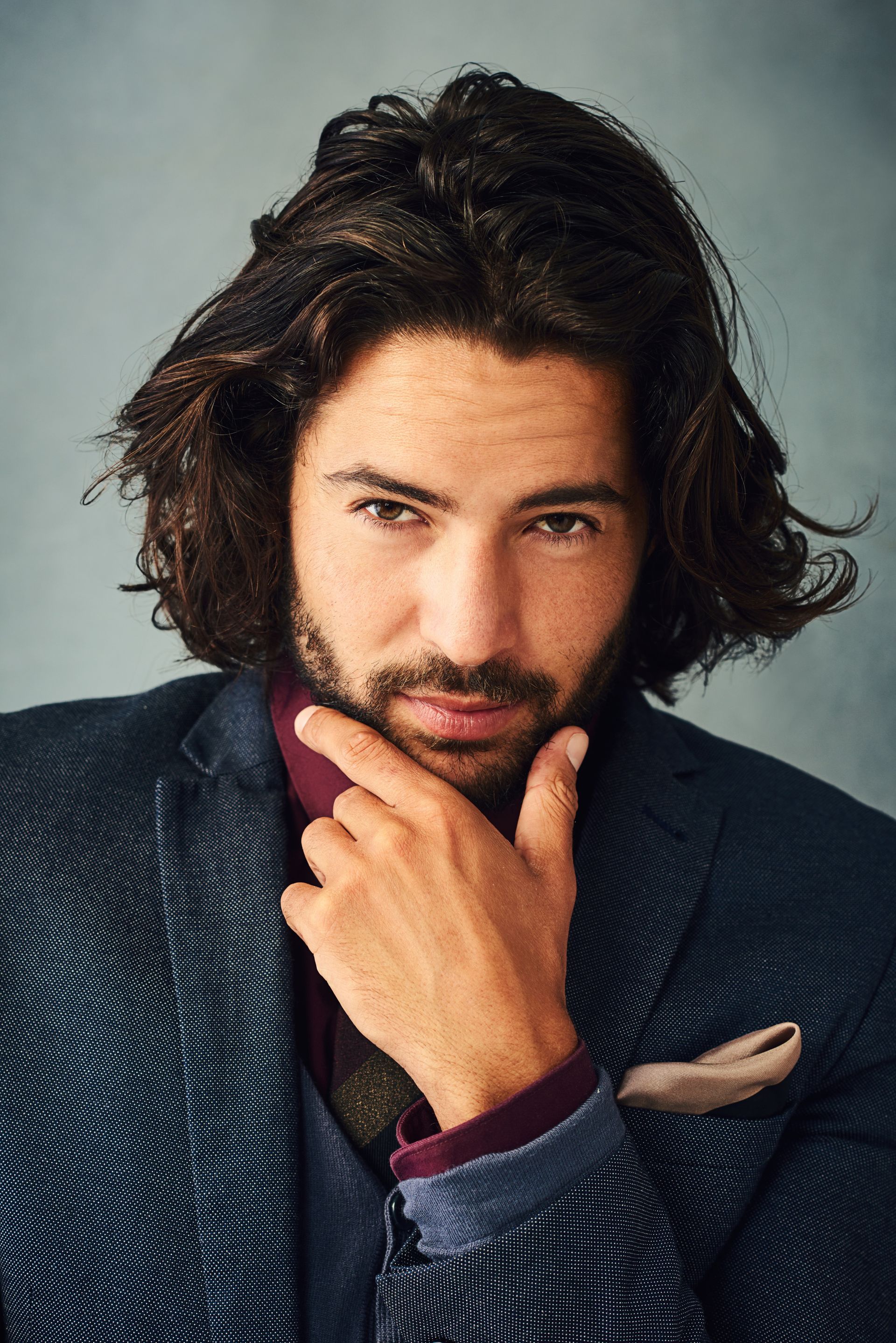 A man with long hair and a beard is wearing a suit and tie.