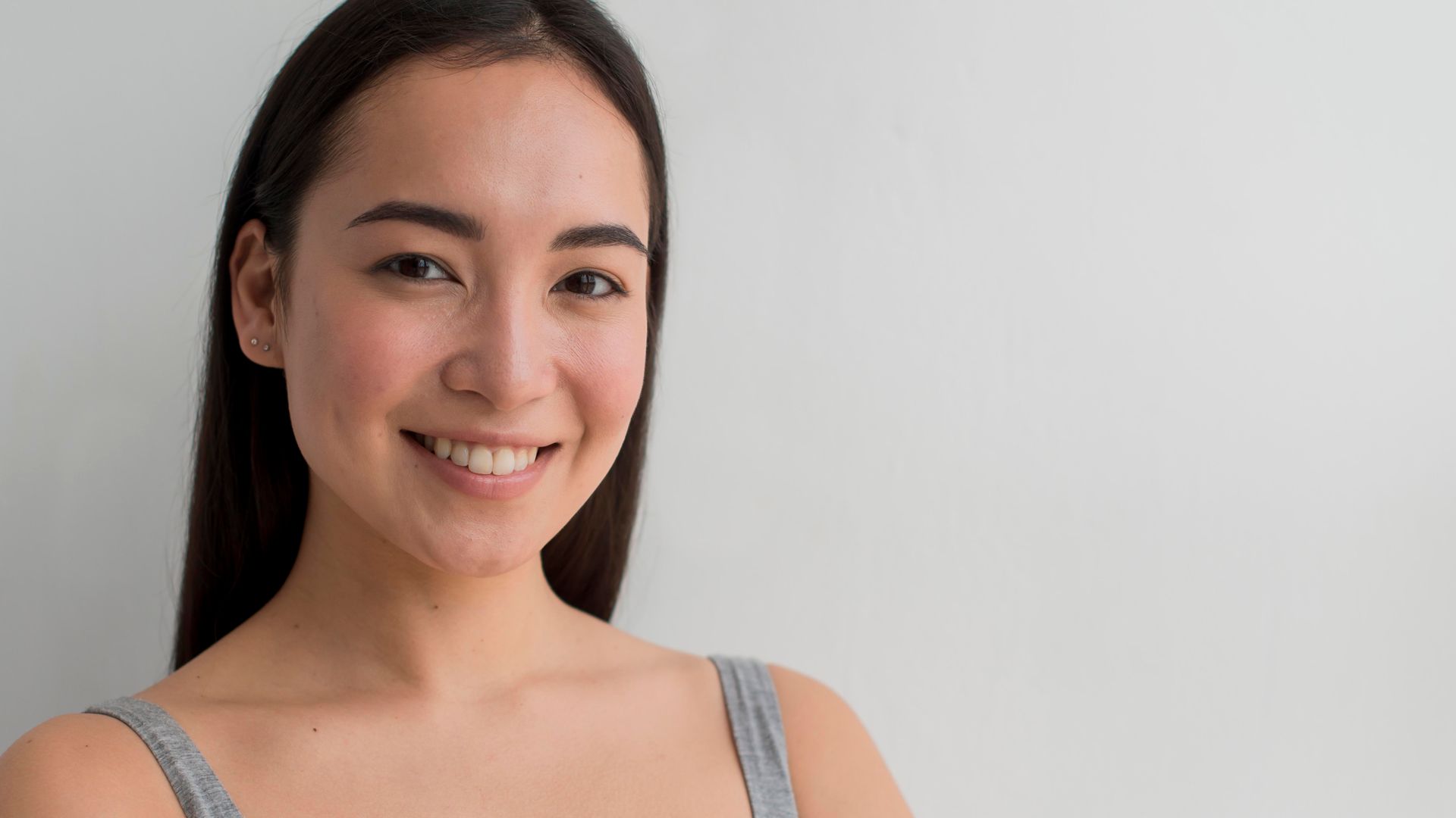 A woman is smiling and looking at the camera while wearing a gray tank top.