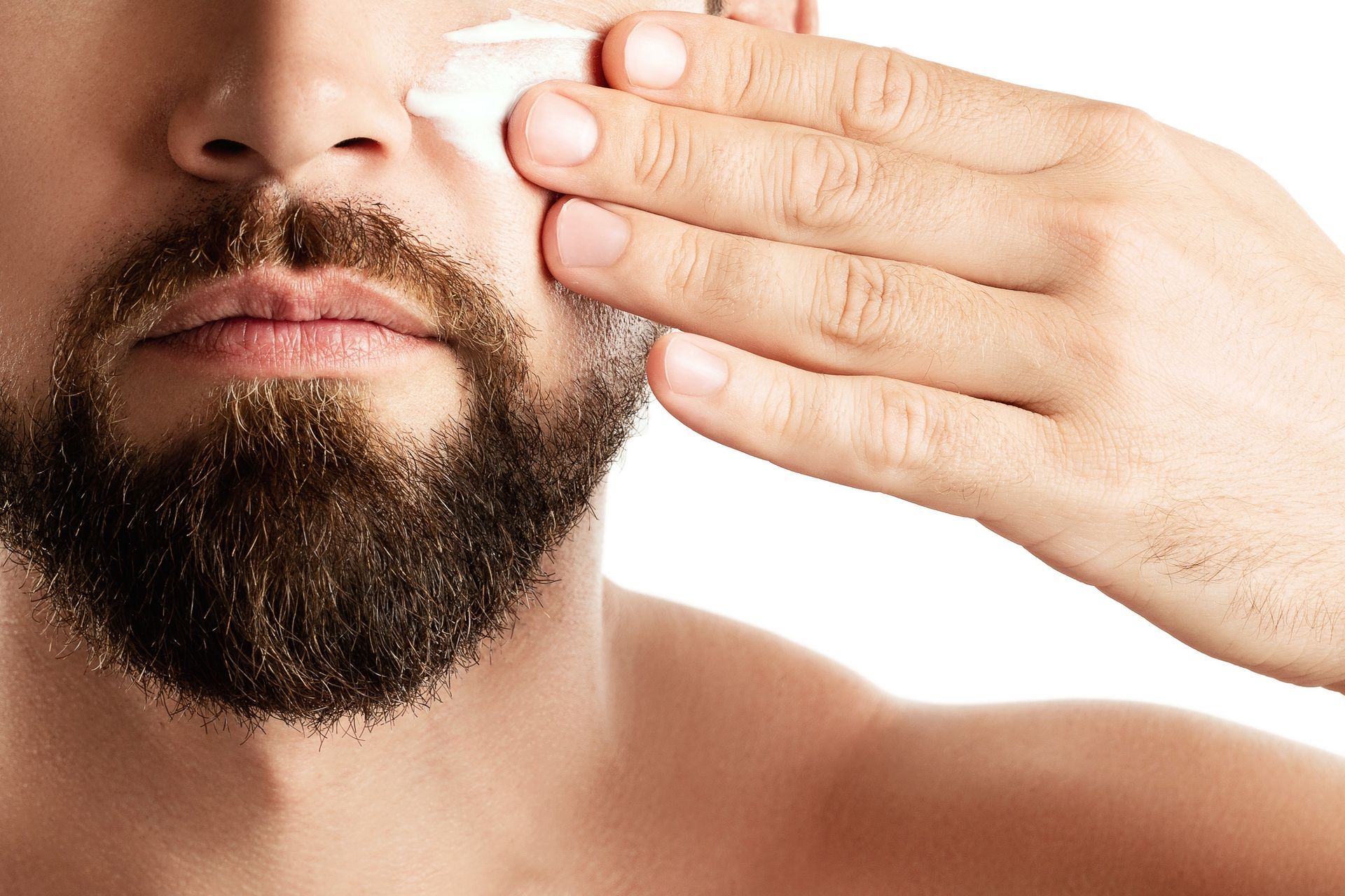 A man with a beard is applying cream to his face.