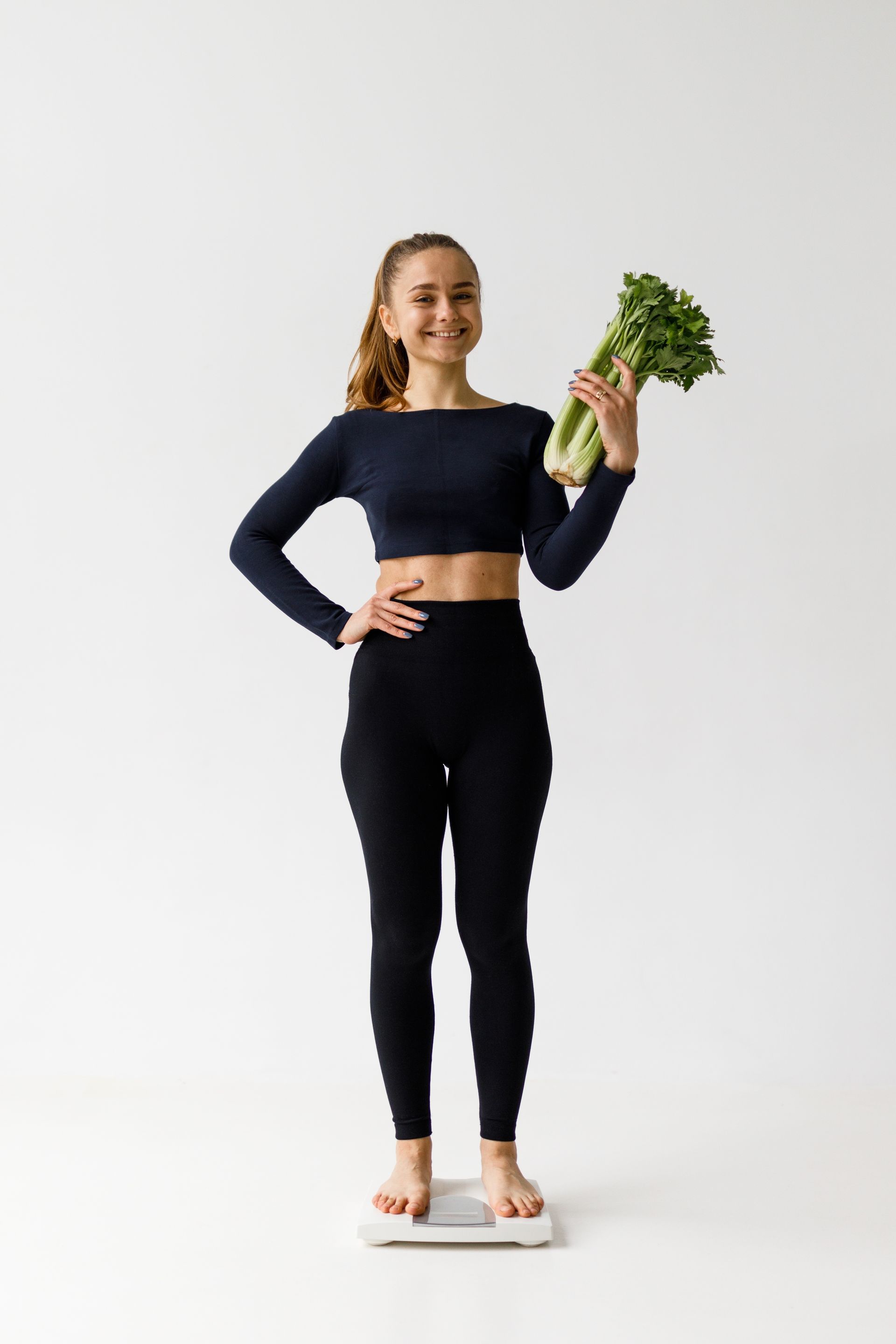 A woman is standing on a scale holding a bunch of celery.