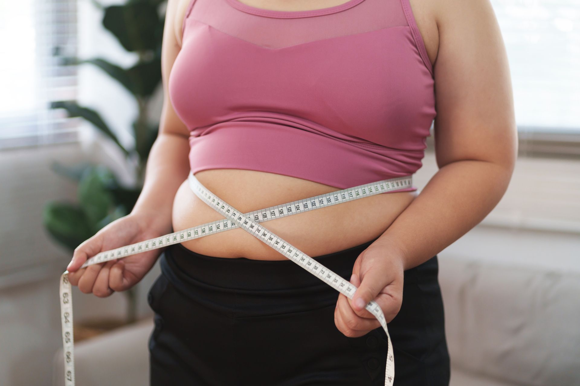 A woman is measuring her waist with a tape measure.