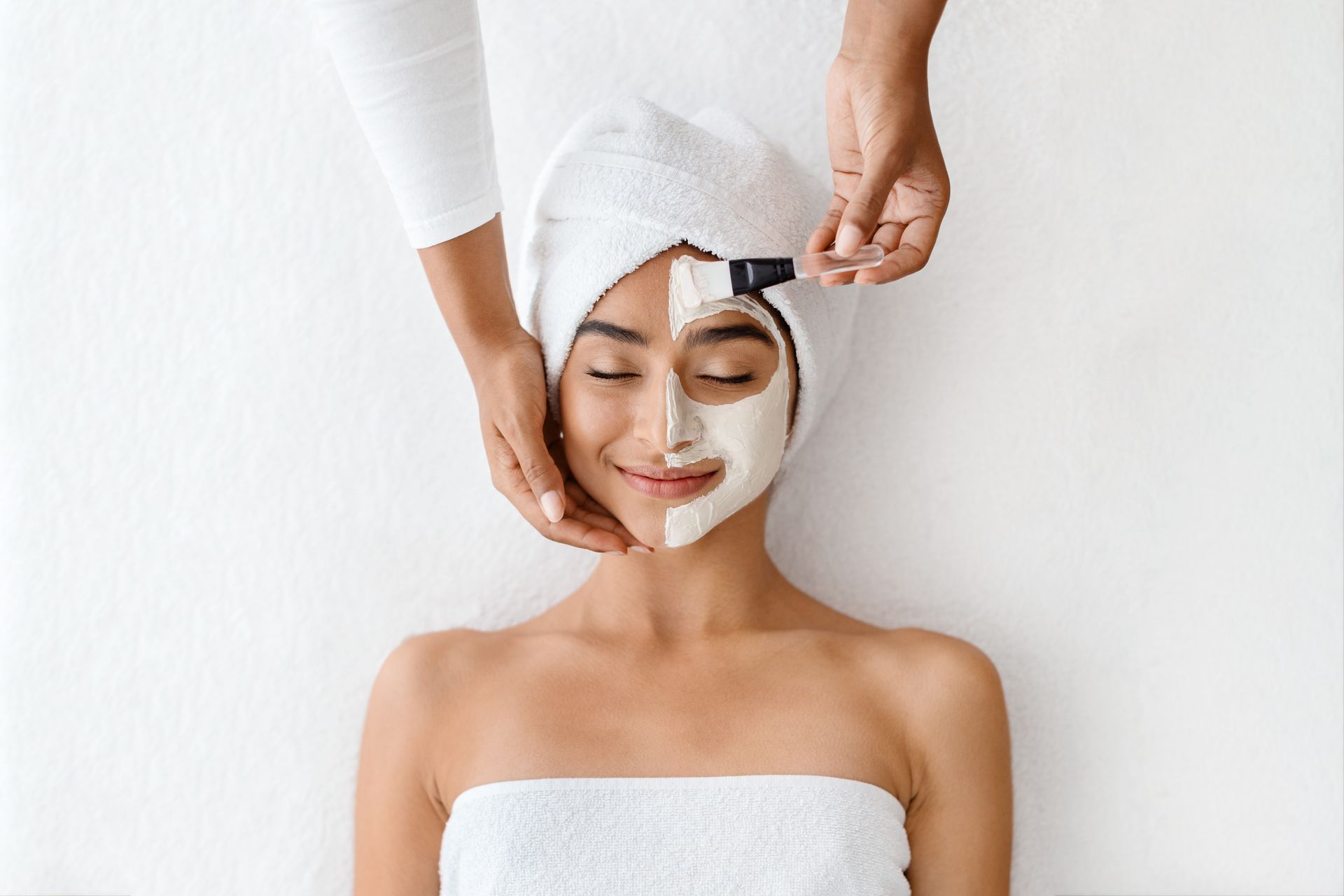 A woman with a towel wrapped around her head is getting a facial treatment at a spa.