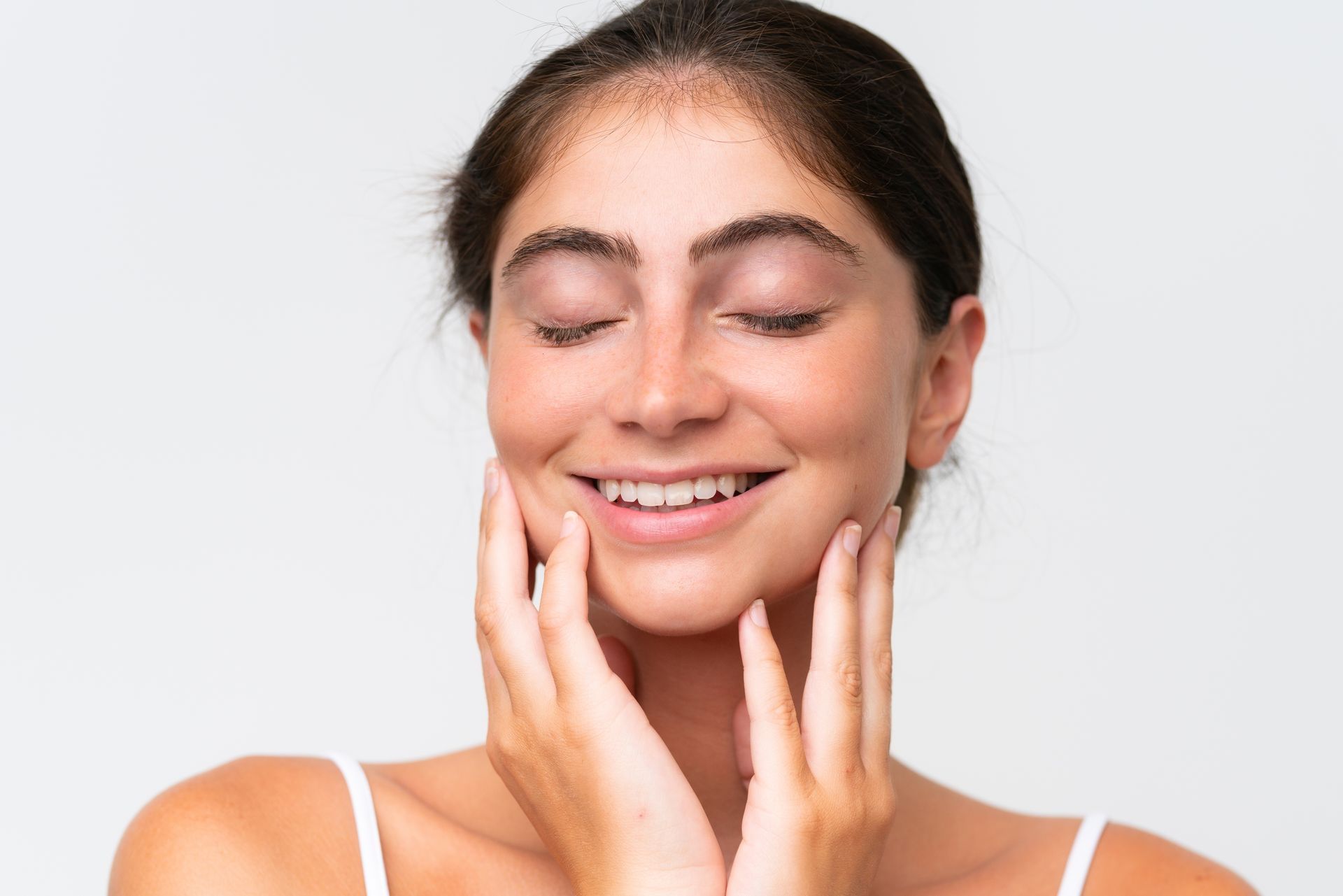 A woman is smiling and touching her face with her hands.