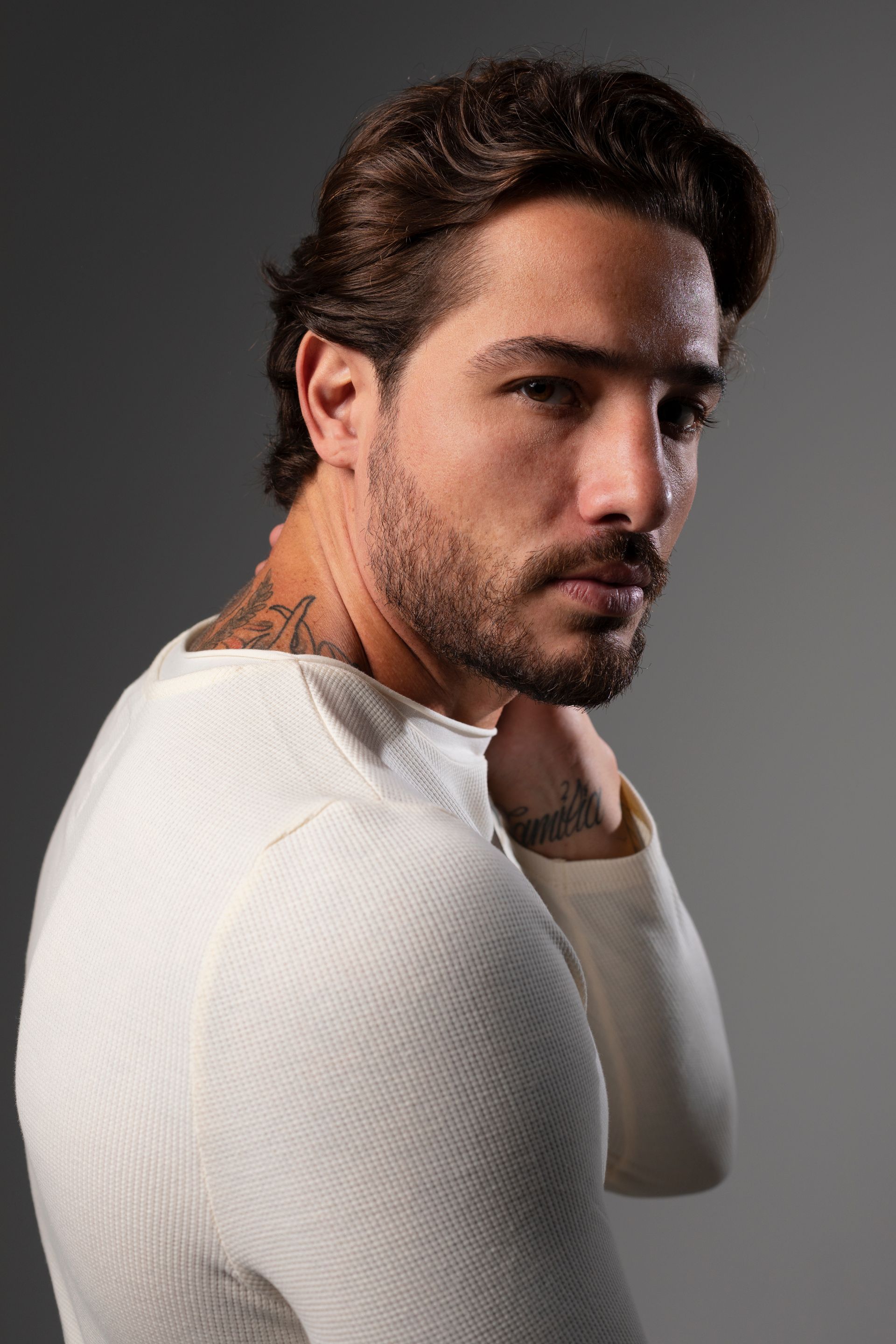 A man with a beard is wearing a white sweater and has a tattoo on his neck.