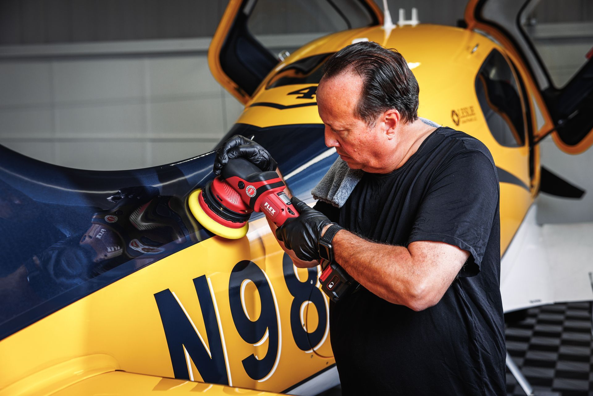 A man is polishing a yellow airplane with the number n98 on it