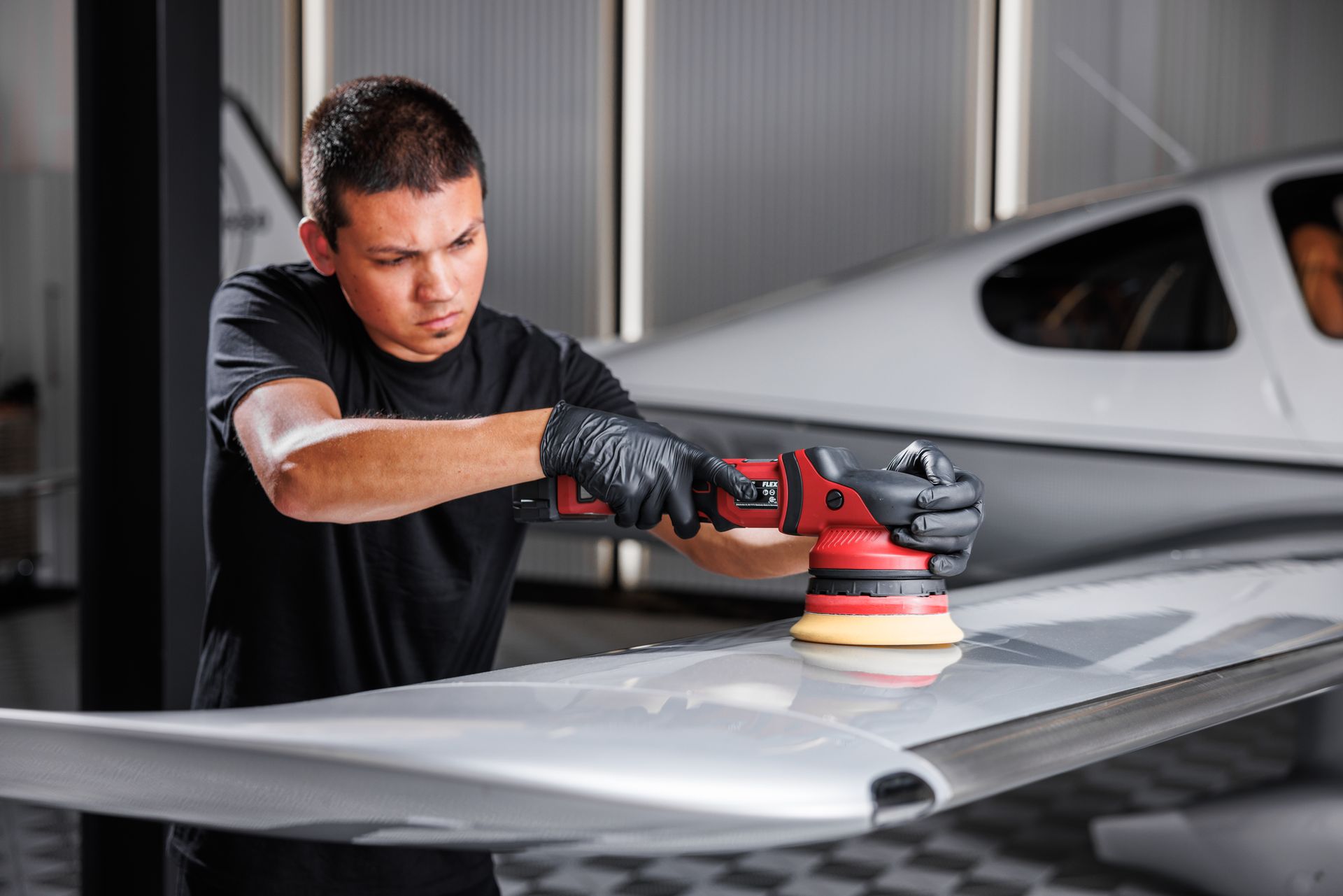 A man is polishing a plane wing with a machine.
