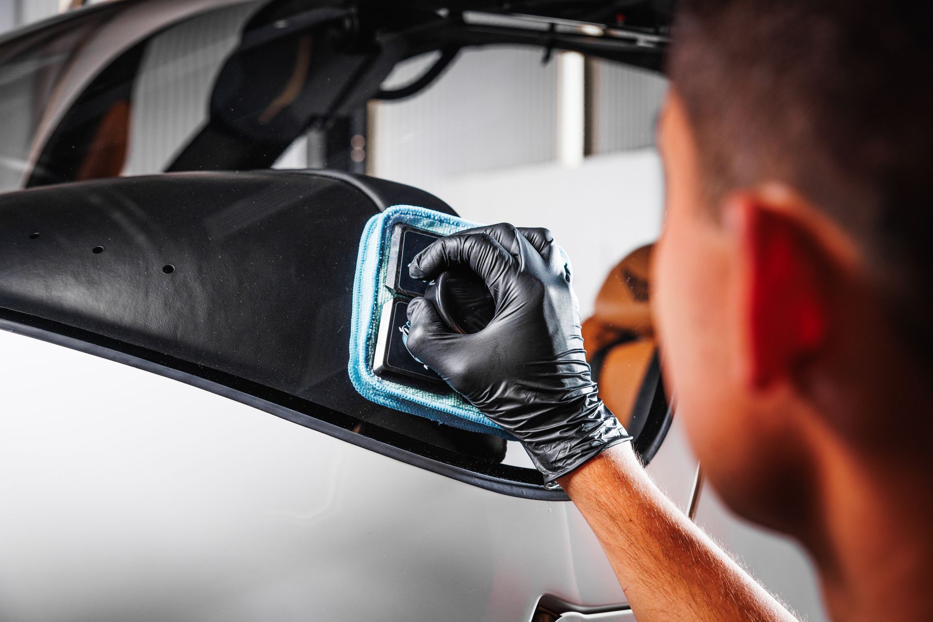 A man wearing black gloves is cleaning a car with a cloth.